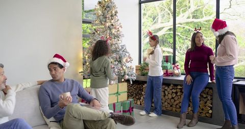 Diverse multigenerational family decorating christmas tree in modern living room with gifts