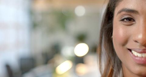 Close-up Indian woman smiling in modern coworking office with warm bokeh and copy space