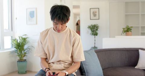 Young man relaxing on living room sofa using smartphone in bright minimalist interior