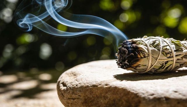 Sunlit sage smudge bundle emitting swirling smoke on garden stone for ritual cleansing