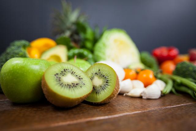 Close-up view of a variety of fresh fruits and vegetables, including kiwi and green apple, on a wooden table. Perfect for use in promoting healthy eating, diet plans, nutrition articles, organic food stores, vegan and vegetarian blogs.