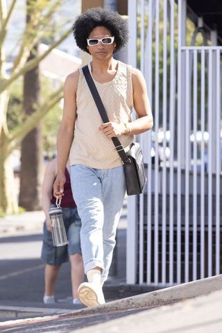 African american man walking city sidewalk in beige sleeveless top and sunglasses