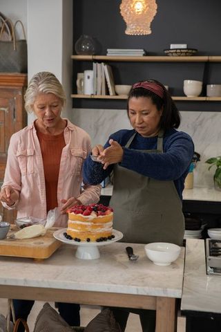 Senior women decorating layered berry cake at marble kitchen island