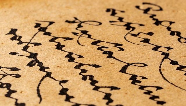 Aged parchment calligraphy macro showing flowing black script on vellum texture