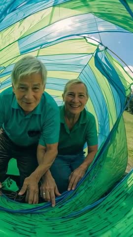Elder couple crawling through blue-green tunnel, laughing, exploring outdoors vertical video