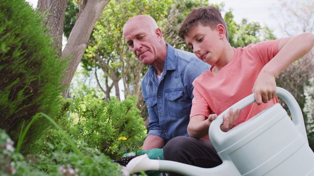 Grandfather and grandson spending quality time together tending to plants in garden. Grandfather looks on while grandson waters the plants, both enjoying a sunny day. Ideal for illustrating themes of family bonding, outdoor activities, gardening hobby, intergenerational relationships, and spending time in nature.