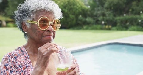 Senior Woman Enjoying Refreshing Drink by Pool in Summer Sun