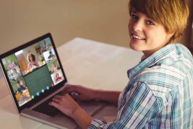 Young woman smiling while participating in virtual meeting on laptop at home, representing remote work, online communication, and virtual collaboration. Suitable for contents on remote work trends, virtual teamwork, home office productivity, and digital business interactions.