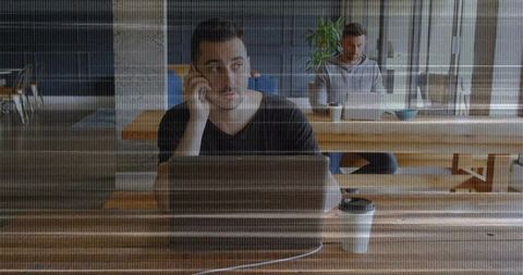 Two Men Sharing Communal Table at Coworking Space Answering Call and Working on Laptop