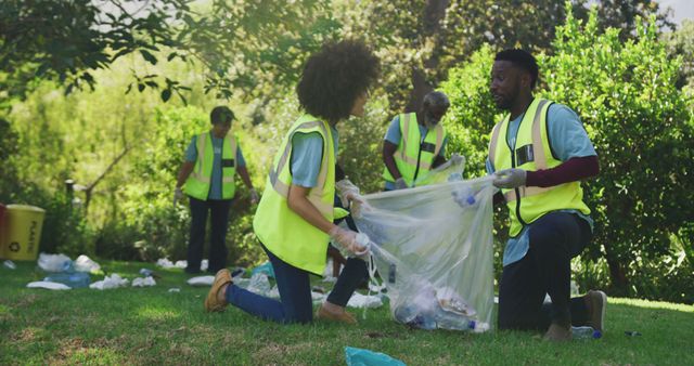 Volunteers wearing yellow reflective vests and gloves engaging in community cleanup efforts by collecting plastic waste and garbage in grassy park area. Ideal for promoting environmental conservation, community initiatives, and teamwork in public service projects.