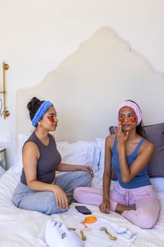 Female friends enjoying at-home skincare session with under-eye patches and face tools