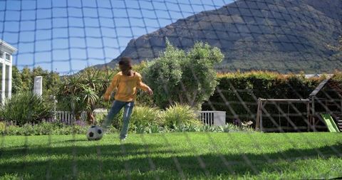 African american boy kicking soccer ball in sunny backyard garden with mountain view