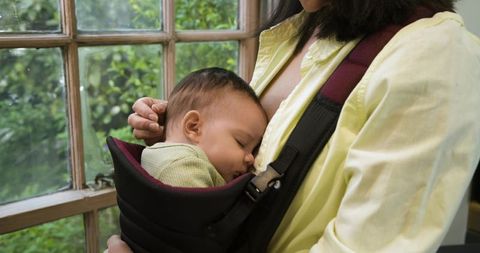 Mother carrying sleeping infant at home near window