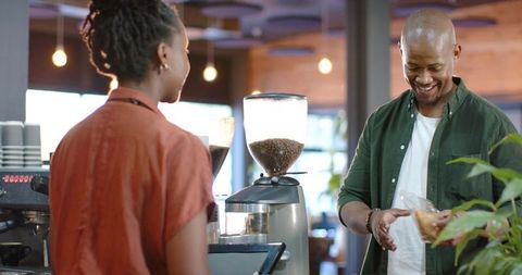 African american barista serving smiling customer at coffeehouse counter with espresso grinder