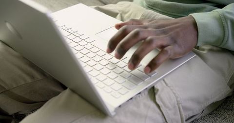 African American man typing on laptop on lap wearing light green sweatshirt