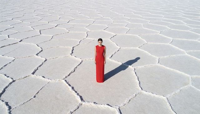 Solitary woman in red gown standing on geometric salt flats casting dramatic shadow