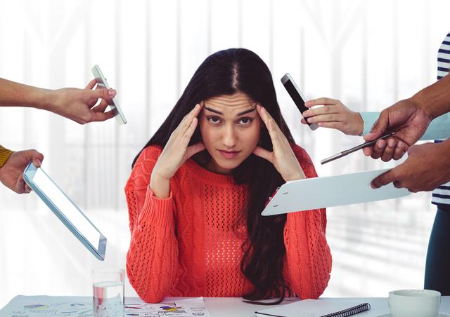 Professional woman sitting at desk with hands on forehead, surrounded by multiple hands holding devices, symbolizing high stress and workload in a busy office setting. Useful for illustrating concepts related to workplace stress, multitasking challenges, and mental health in corporate environments.
