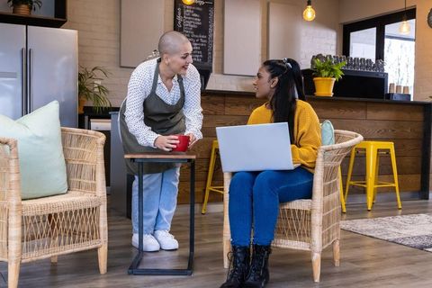 Barista handing red cup to customer working on laptop in cozy rustic cafe lounge