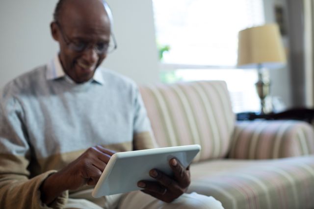 Smiling senior man using tablet while sitting on sofa at home