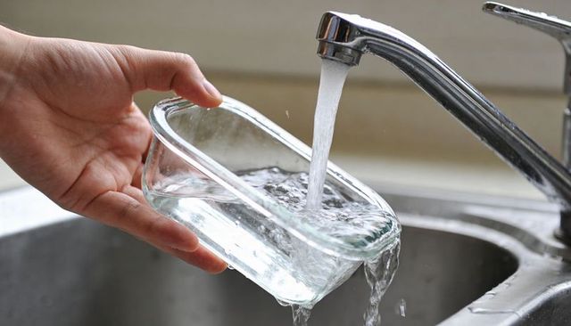 Hand holding rectangular glass container filling with running water from chrome kitchen faucet