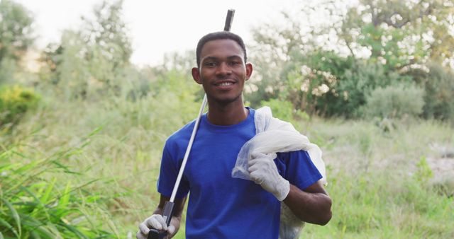Portrait of a male African American volunteer cleaning up a river in the countryside, holding a rubbish bag, smiling and looking at camera. Ecology and social responsibility in a rural environment.