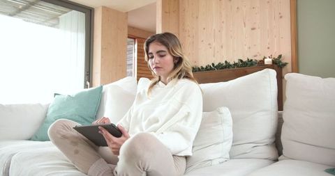 Woman Relaxing on Sofa Holding Tablet in Cozy Living Room