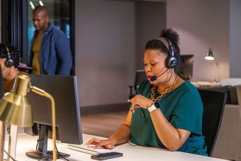 Customer support agent wearing headset and smartwatch working at open-plan office desk
