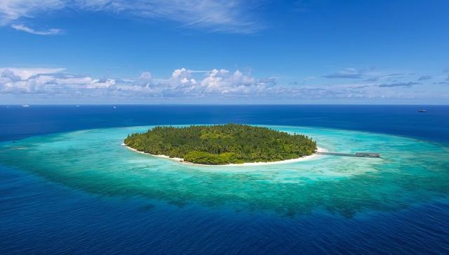 Circular tropical island sitting in turquoise lagoon with white sand beach and pier