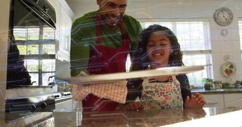 Father teaching daughter baking in sunlit kitchen removing tray with oven mitt smiling