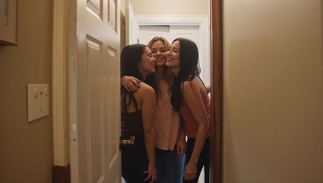 Three friends hugging in narrow doorway, smiling and leaning together in cozy hallway