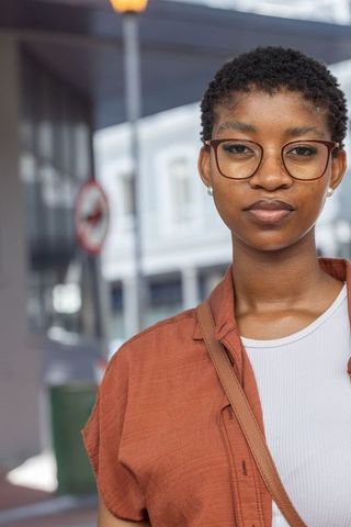 African woman wearing round glasses standing confidently on urban sidewalk with handbag