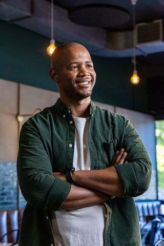 Confident african american entrepreneur standing with arms crossed smiling in modern cafe