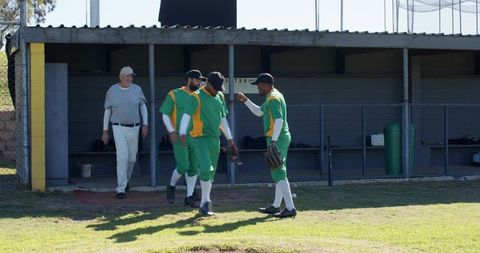 Diverse baseball teammates and senior coach gathering at dugout preparing for game