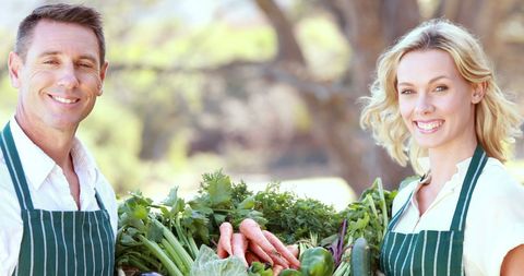 Cheerful Vendor Couple Presenting Fresh Vegetables at Local Market Outdoors