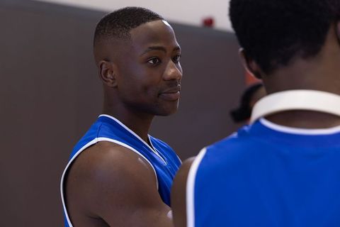African american basketball player listening on sideline in blue jersey, team focused