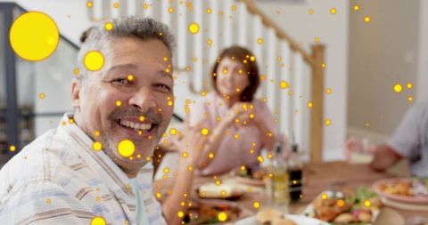 Smiling mature man enjoying multigenerational family dinner with festive bokeh lights