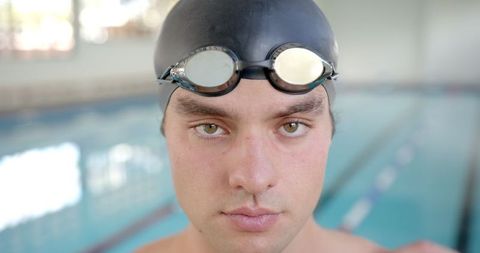 Focused Male Swimmer Preparing with Goggles in Indoor Pool