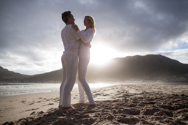 Mature couple enjoying a romantic moment on a beach at sunset. They are dancing and smiling, creating a joyful and loving atmosphere. Ideal for use in advertisements, travel brochures, lifestyle blogs, and articles about romance, senior living, and outdoor activities.