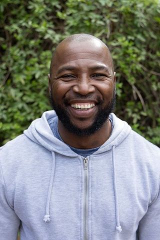 African american man smiling in garden wearing gray hoodie, closeup outdoor portrait