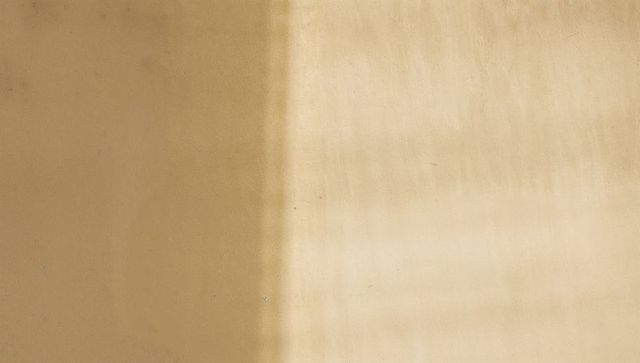 Displaying vertical light band crossing textured beige wall with patina and streaks