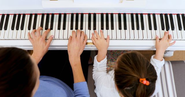 Overhead of caucasian mother and daughter playing piano together. Music, childhood, motherhood, togetherness, learning, teaching, education and domestic life, unaltered.