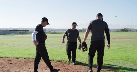 Mature baseball teammates practicing on sunny infield discussing strategy holding gloves and wearing