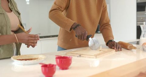 Young couple baking together cutting pastry dough on bright modern kitchen island