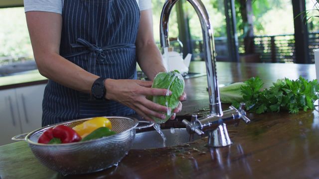 A pregnant woman is washing a variety of fresh vegetables, including bell peppers and lettuce, under a modern kitchen faucet. The scene emphasizes healthy living and the wholesomeness of home-cooked meals. This can be used for content related to nutrition during pregnancy, cooking tips for expectant mothers, or healthy lifestyle promotional materials.