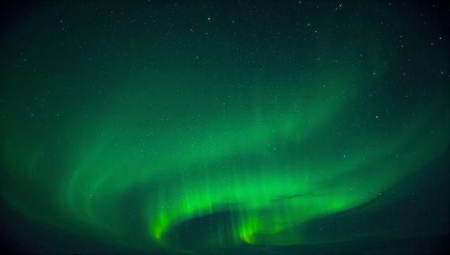 Dancing green aurora borealis curtains over starry northern sky with silhouetted horizon