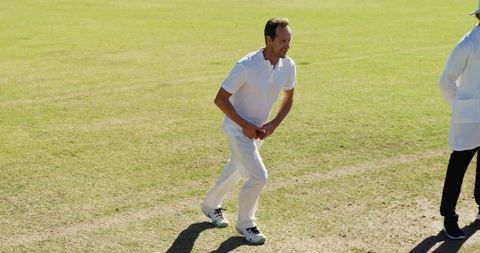 Cricketer running to bowl on green pitch in uniform