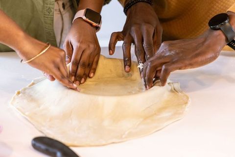 Friends shaping pie crust together in kitchen, teamwork kneading dough with smartwatches