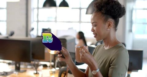 Holding mug and checking smartphone in bright modern open-plan office, workplace productivity