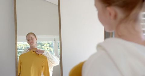 Woman Evaluating Mustard Yellow Sweater in Minimalist Interior