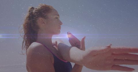 Woman stretching arm across chest at sunlit beach with lens flare and athletic focus
